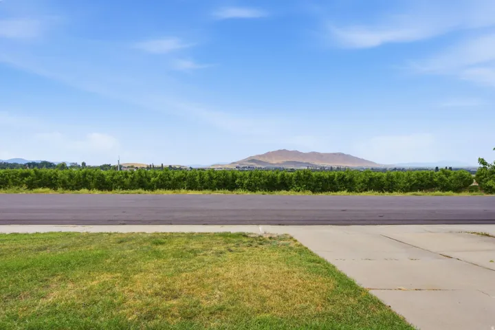 Lush green landscaping with a concrete walkway, asphalt paving, and distant mountainous terrain