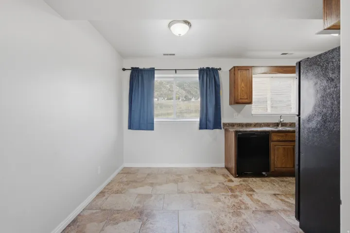Kitchenette featuring wood-finish cabinetry, a black dishwasher, and a stainless steel sink