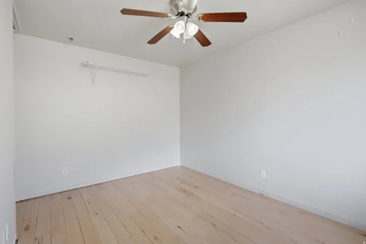 Light wood-finish flooring, white walls, and a ceiling fan with integrated lighting