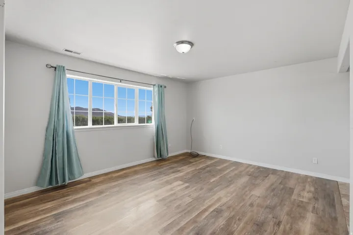 Spacious room featuring wood-finish flooring, a large multi-pane window, and a flush-mount ceiling light fixture