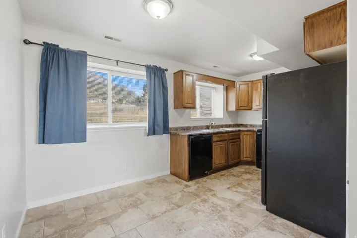 Kitchen featuring wood cabinetry, black appliances, solid surface countertops, and tile flooring