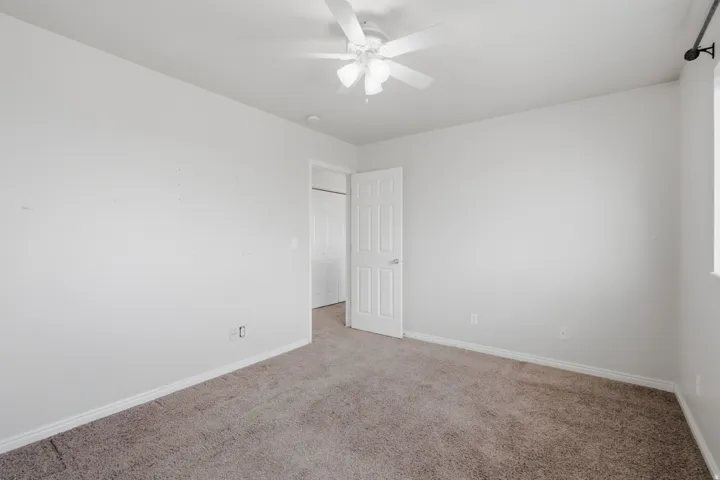Neutral color palette throughout, featuring a ceiling fan, window with curtain rod, and carpeted flooring