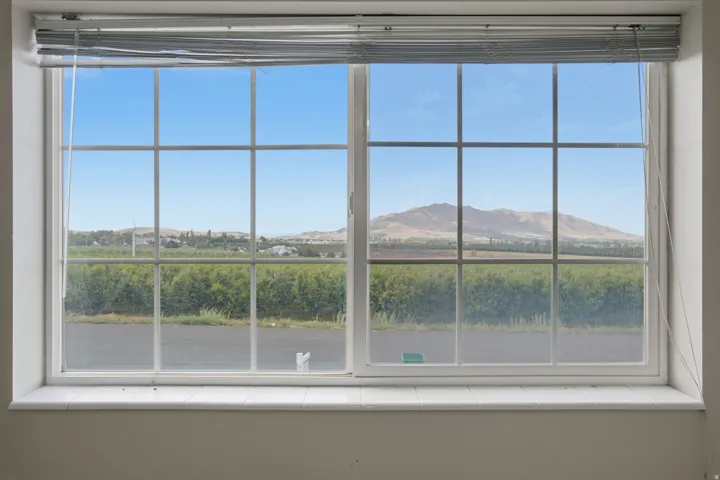 Gridded window with a tiled sill, offering expansive scenery of distant mountains and a field