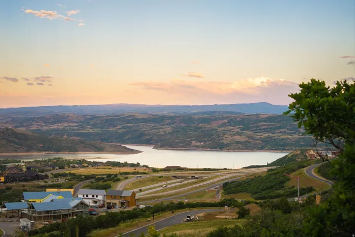 Expansive water body surrounded by undulating hills and distant mountains, featuring a developed residential area with multiple structures and winding roads
