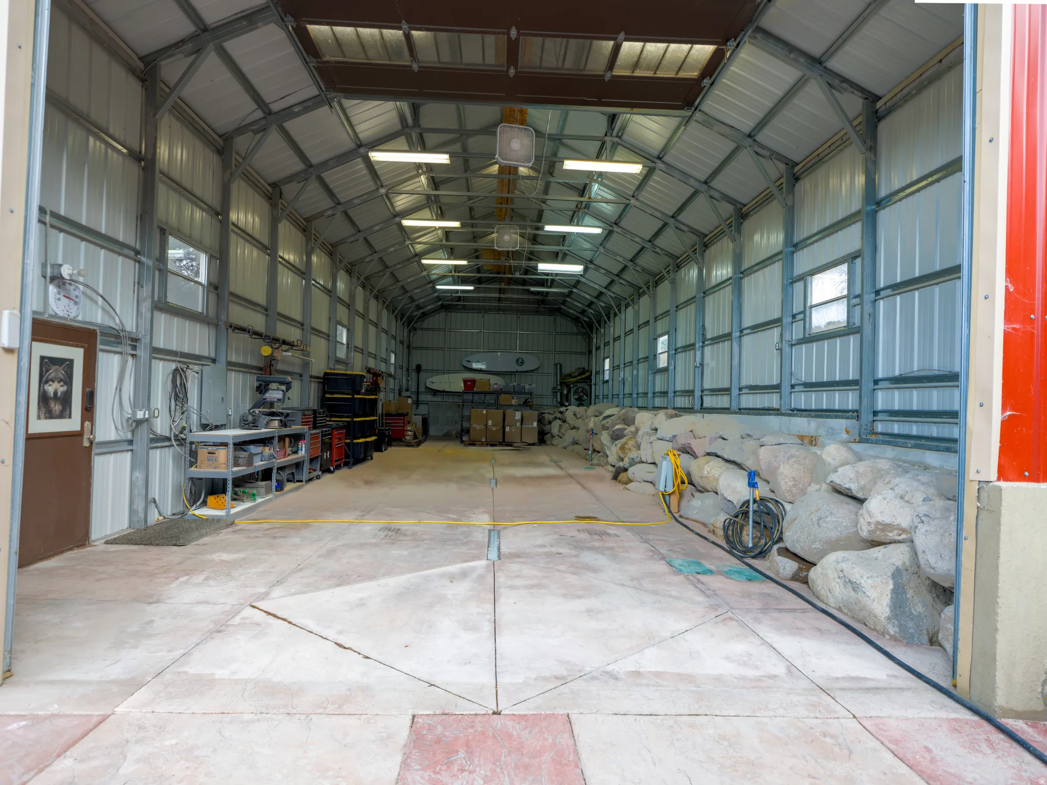 Large metal structure featuring a concrete floor, exposed metal framing, and multiple overhead lights