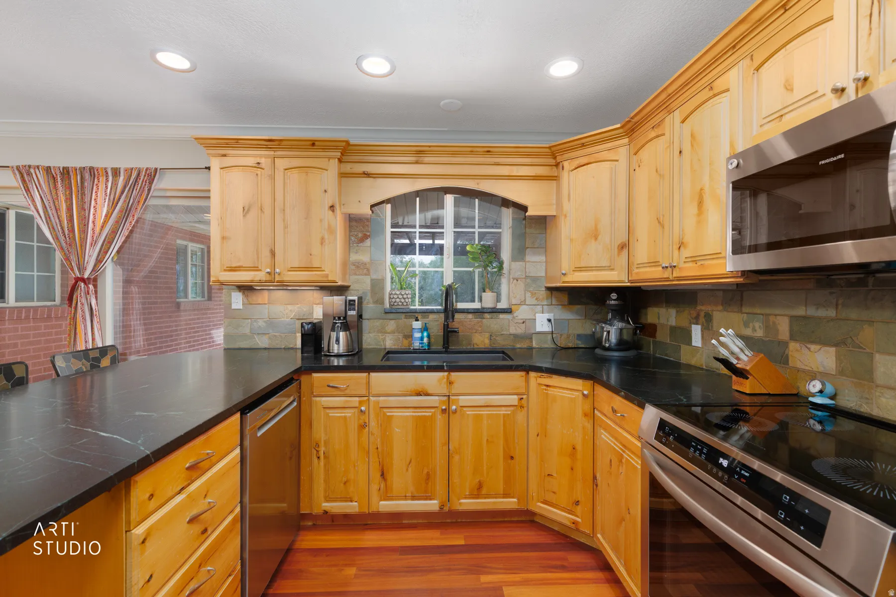 Kitchen featuring wood-finish cabinetry, dark countertops, a tile backsplash, and stainless steel appliances