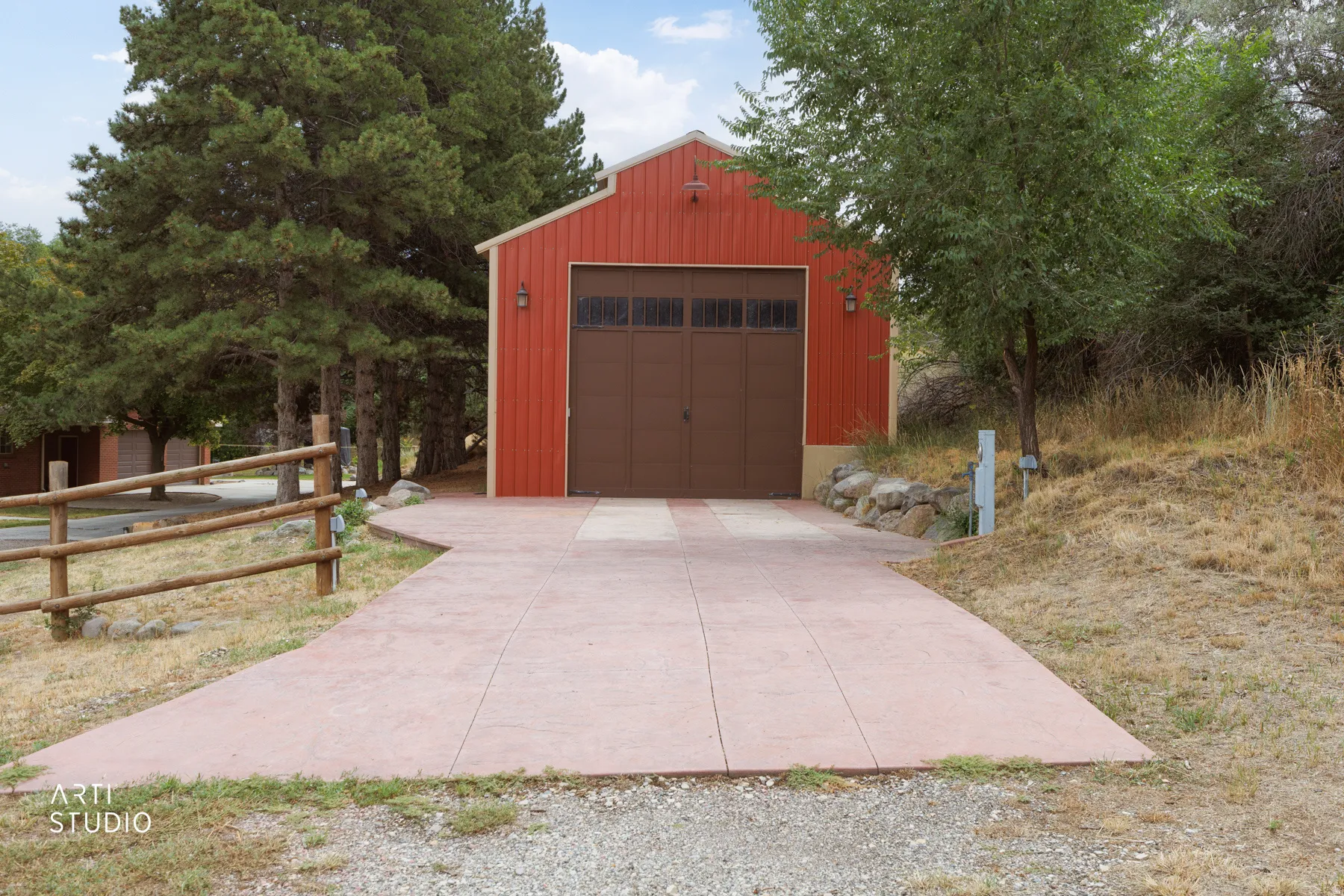 Red exterior structure with a brown garage door featuring upper window panels, sconce lighting, and a concrete driveway