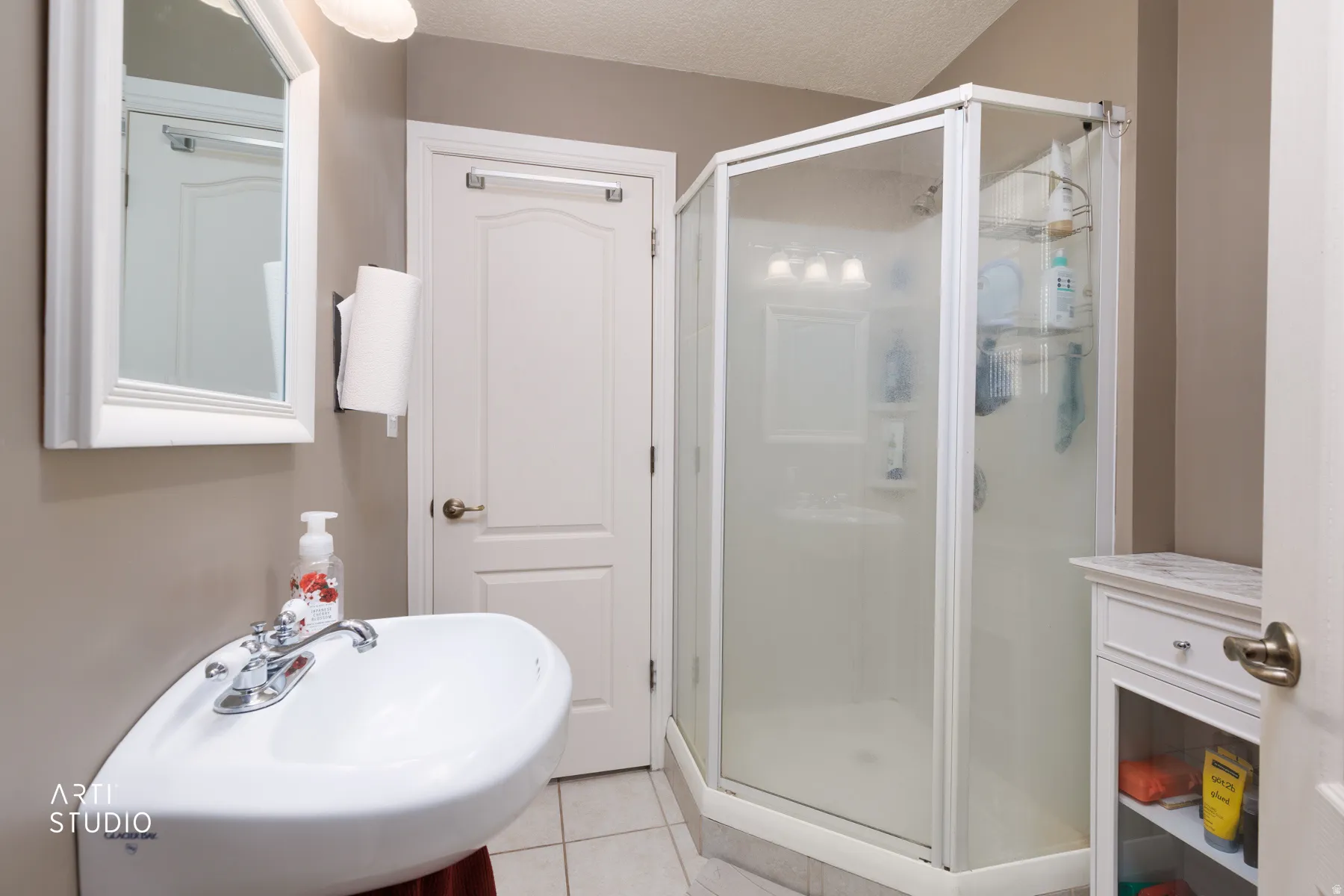 White pedestal sink with chrome faucet, framed mirror, and a corner shower enclosure