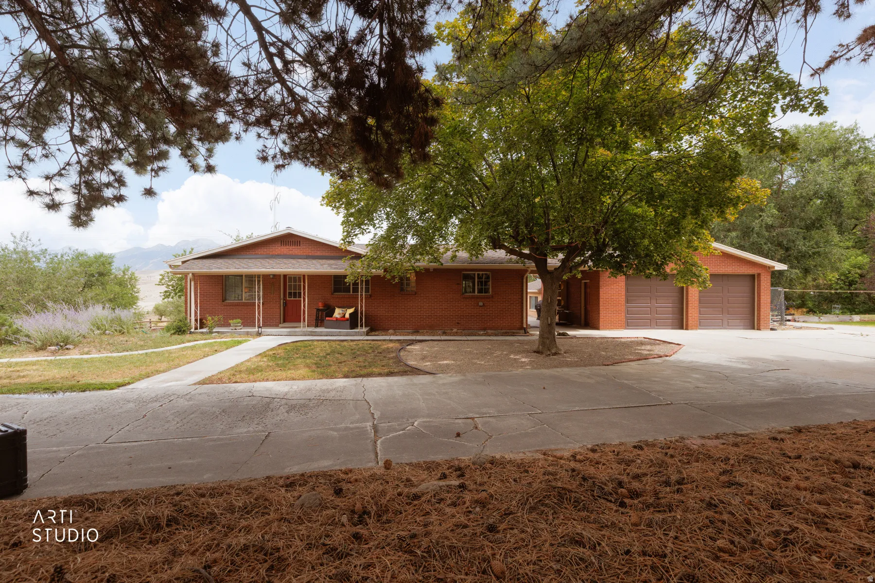 Brick exterior with a covered porch, an attached garage, a mature tree, and a concrete driveway