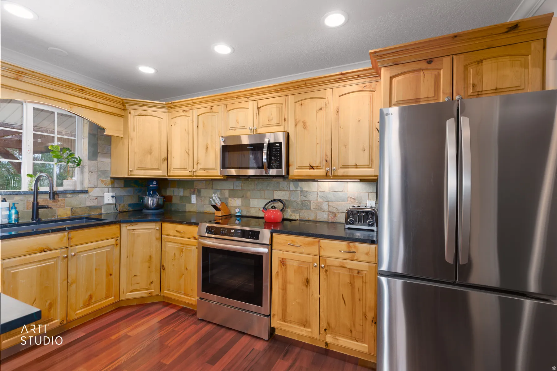 Kitchen featuring wood cabinetry, dark countertops, stainless steel appliances, a tiled backsplash, and wood-finish flooring