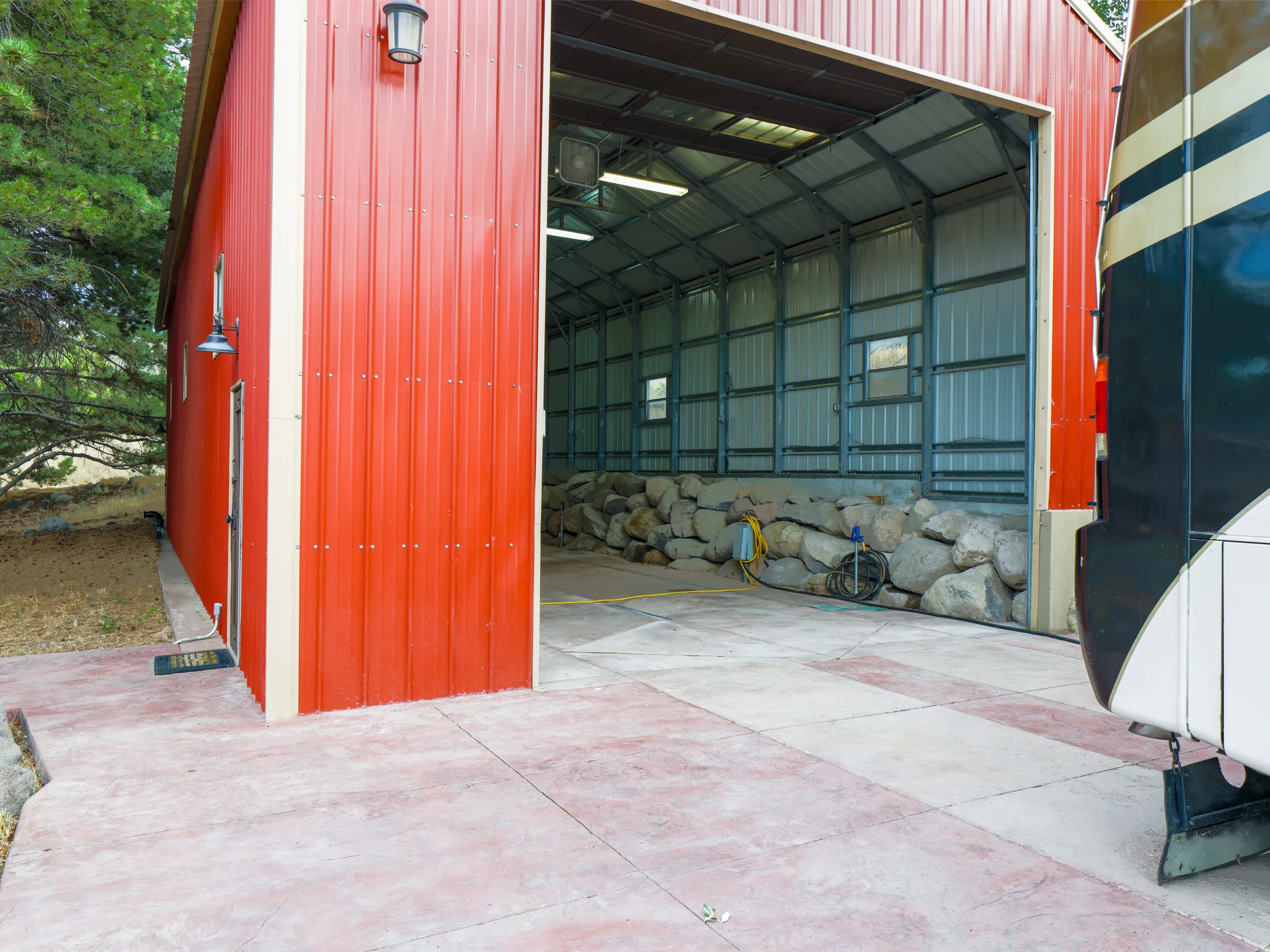 Red metal-sided building with a large overhead door, interior metal framing, and concrete flooring