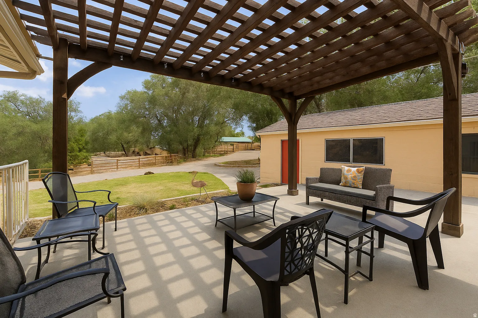 Expansive concrete patio featuring a wooden pergola, mature trees, and an additional detached structure with a red door