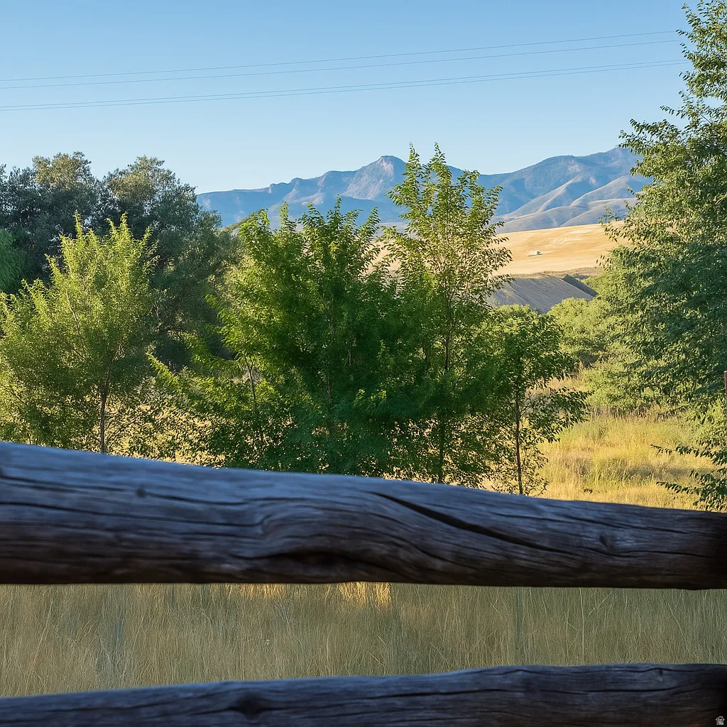 Property featuring a split-rail fence, mature trees, expansive fields, and distant mountains