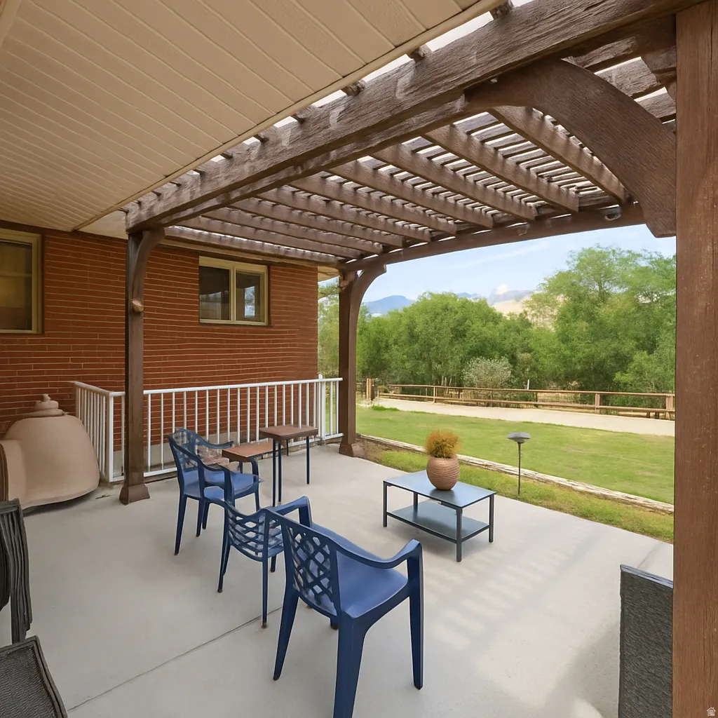 Expansive concrete patio with a wood pergola structure, brick exterior, and white railing