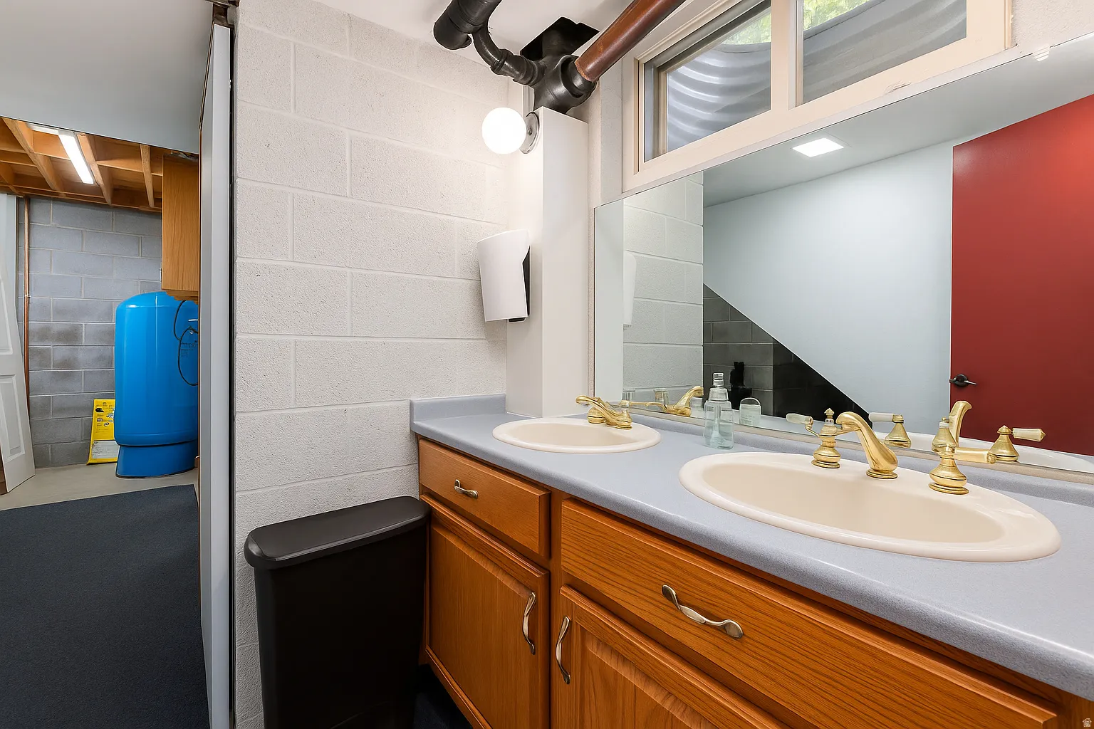 Dual vanity with light wood-finish cabinetry, gold-finish faucets, and an expansive mirror
