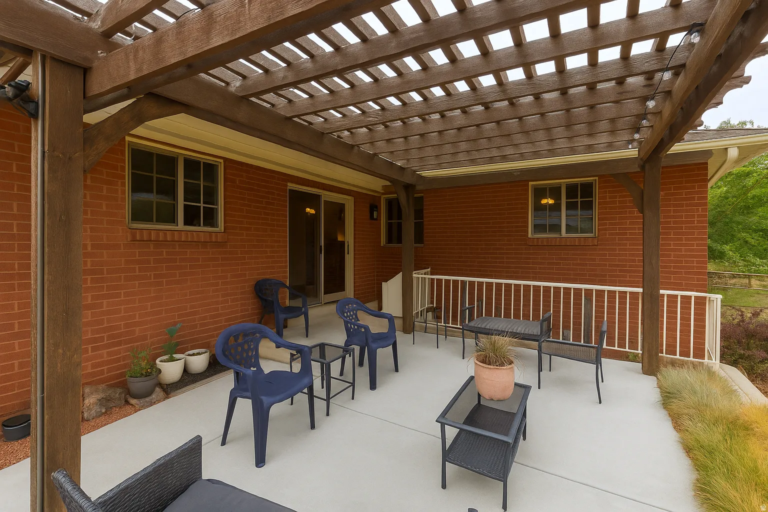 Expansive outdoor patio featuring a wood pergola, concrete surface, brick exterior, and white railing