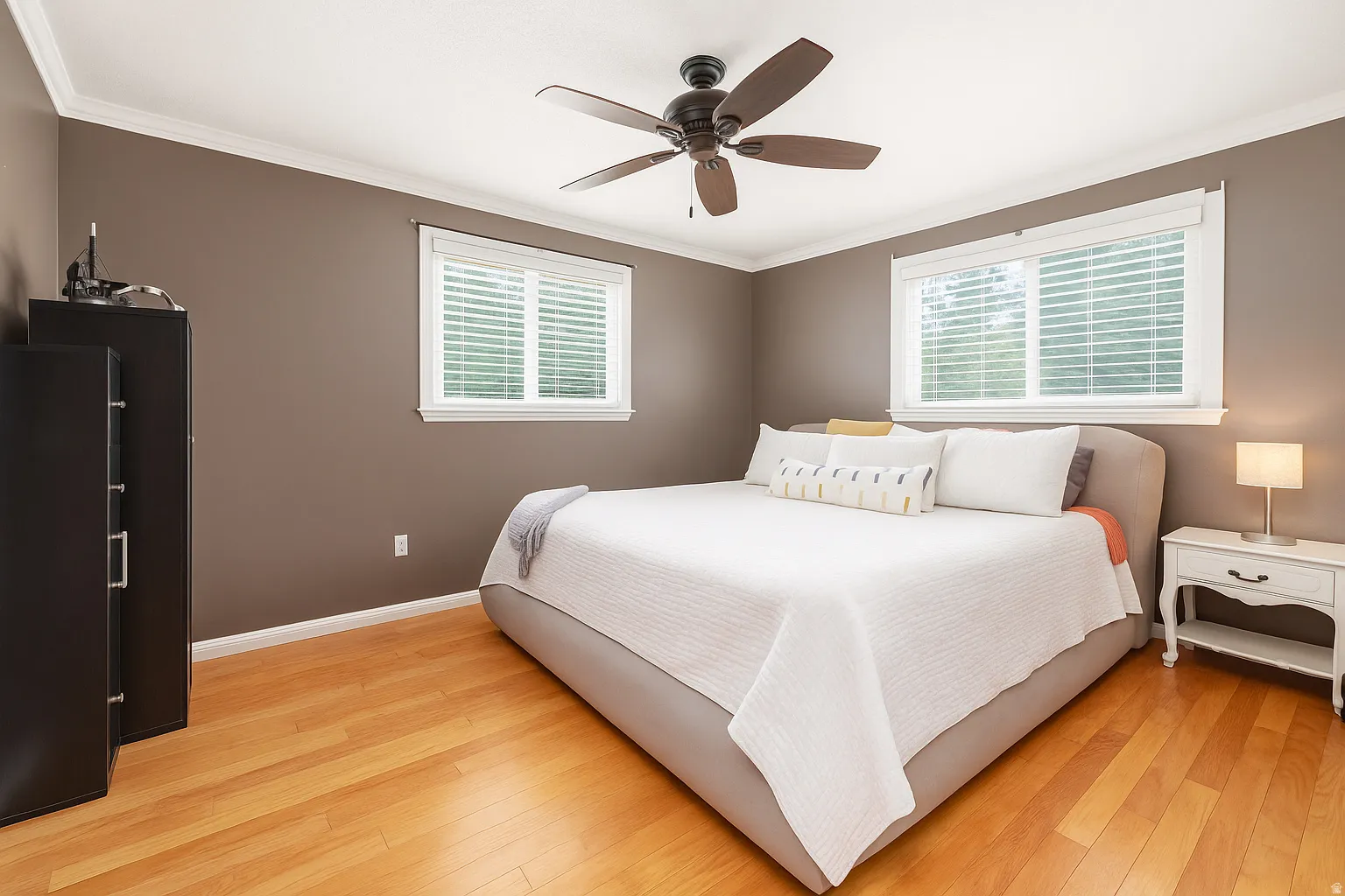 Hardwood flooring throughout, with two windows providing natural light, crown molding, and a ceiling fan