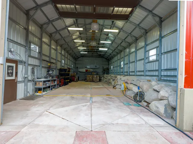 Large metal structure featuring a concrete floor, exposed metal framing, and multiple overhead lights