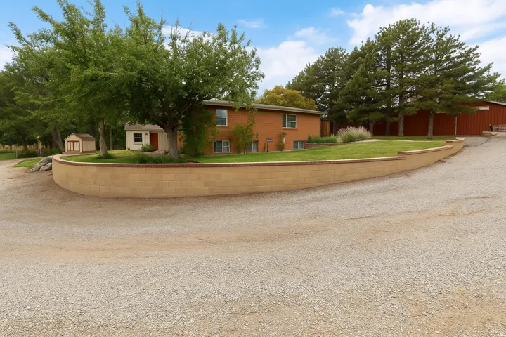 Brick exterior residence with a gravel driveway, retaining wall, and mature trees