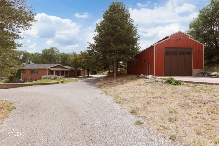Gravel driveway leading to a red barn-style auxiliary structure with a large garage door, and a brick residence with a covered front porch and multi-pane windows