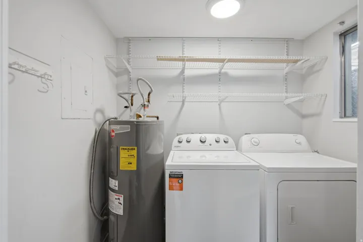 Laundry area featuring a top-load washer, front-load dryer, wall-mounted wire shelving, and a window