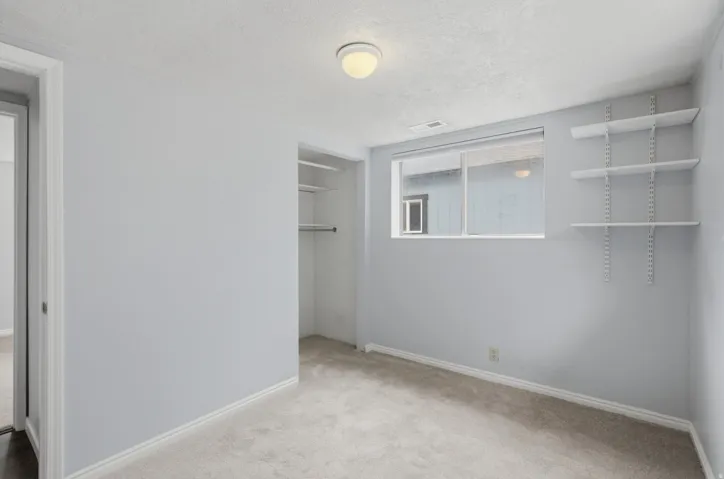 Neutral tone walls, carpeted flooring, built-in closet with hanging rod and shelving, adjustable wall-mounted shelving, and a window with blinds
