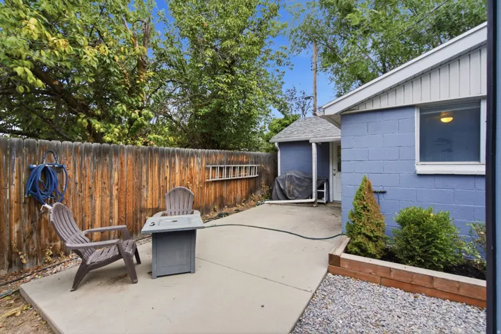 Private fenced yard with concrete patio, mature trees, a detached shed, and a raised planter bed with gravel