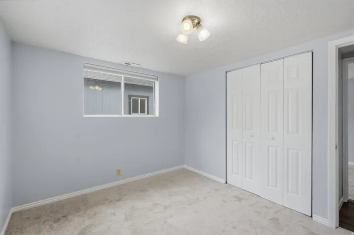 Recessed window, white bi-fold closet doors, wall-mounted light fixture, and light-toned carpet flooring