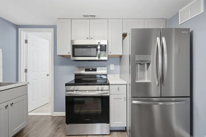 Stainless steel appliances, light gray cabinetry, wood-finish flooring, and light-toned countertops
