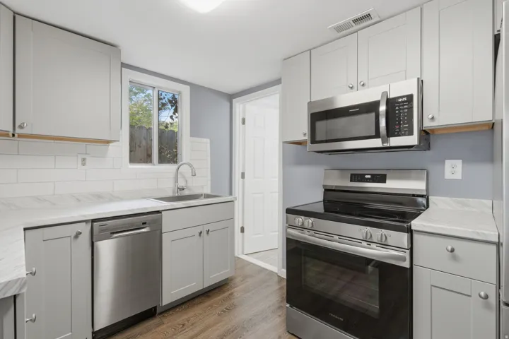 Kitchen featuring stainless steel appliances, light gray cabinetry, white subway tile backsplash, and wood-finish flooring