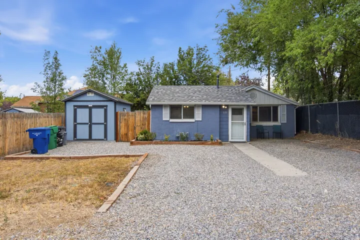 Blue siding exterior with white trim, a gravel driveway, a concrete walkway, a detached storage shed, and wood fencing