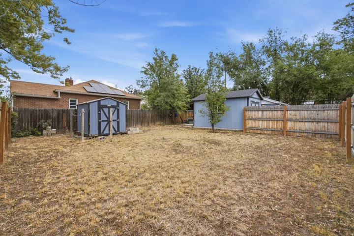 Expansive fenced backyard featuring two storage sheds, a brick exterior, and solar panels