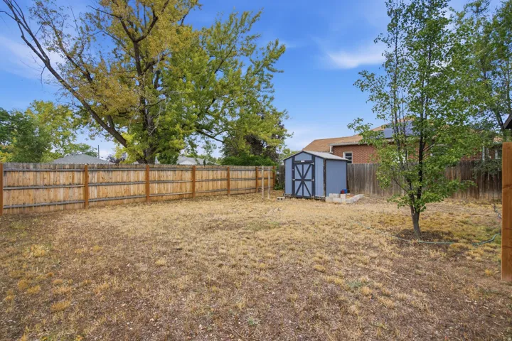 Enclosed backyard featuring a wood fence, mature trees, and a storage shed