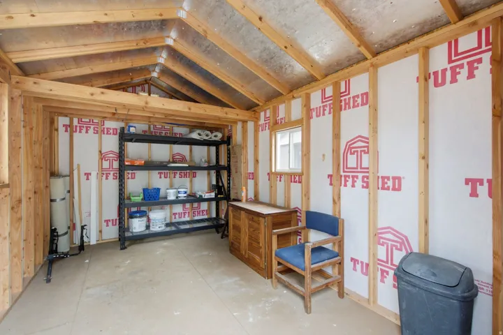 Exposed wood framing with vaulted ceiling, window for natural light, and concrete flooring