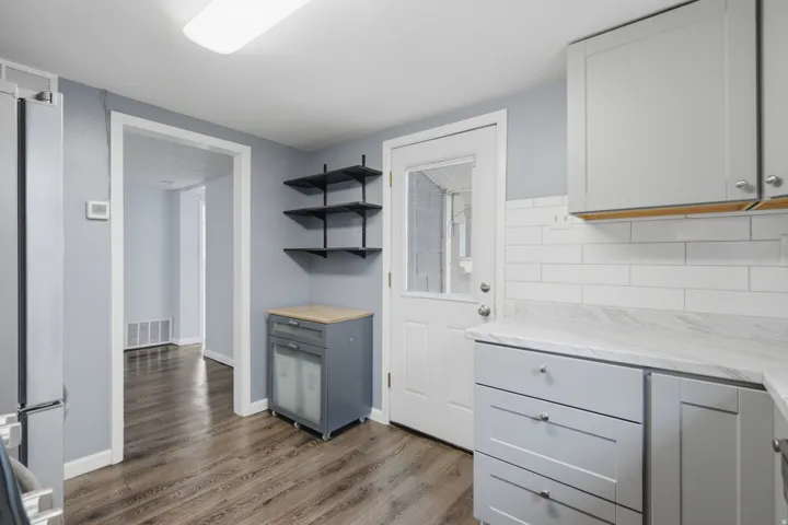 Wood-finish flooring, light grey cabinetry, white subway tile backsplash, and a modern ceiling light fixture