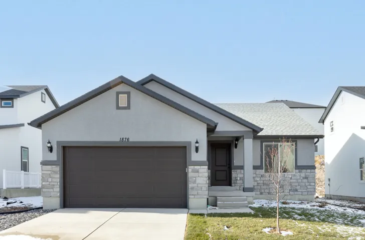 Contemporary stucco exterior with stone accents, attached garage, covered entryway, and front yard landscaping