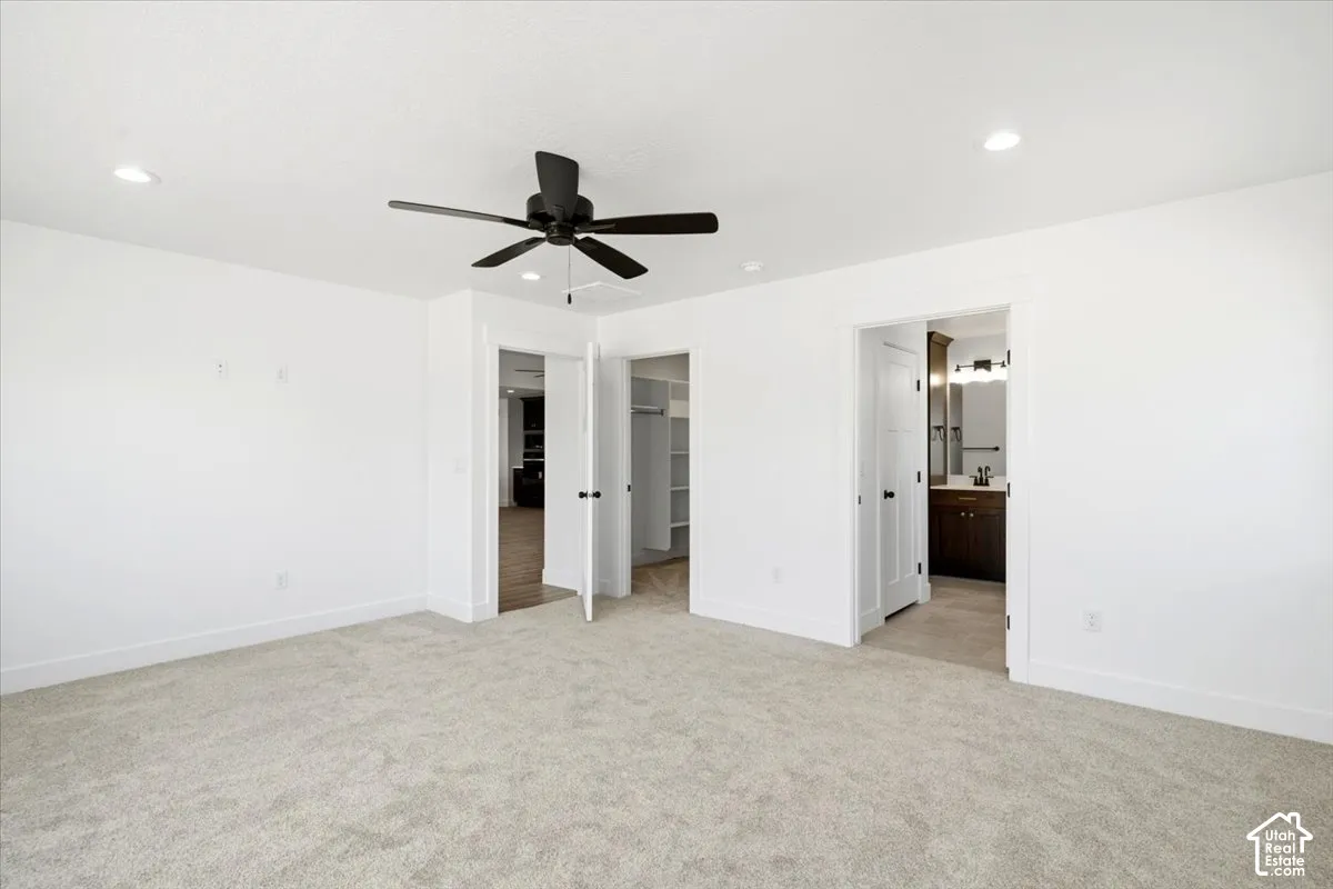 Spacious room featuring light-colored carpeting, white walls, recessed lighting, and a matte black ceiling fan