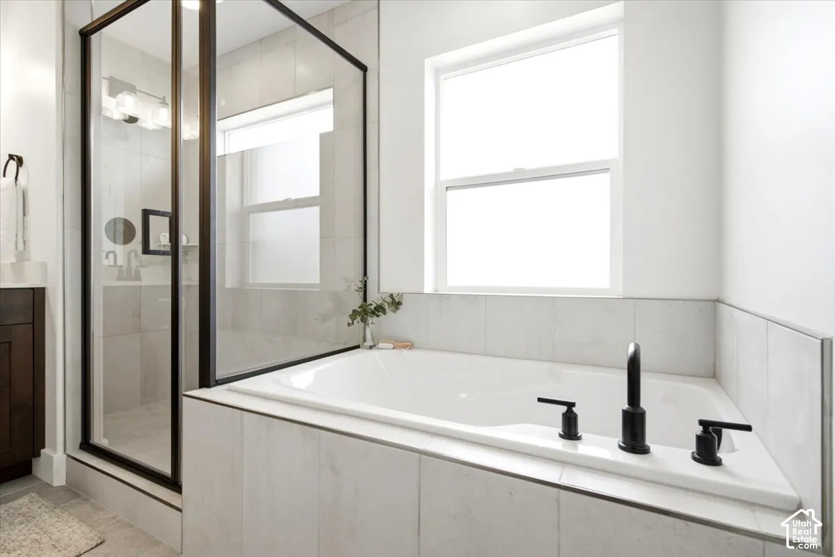 Built-in soaking tub with matte black fixtures, white tile surround, and a clear glass shower enclosure with black trim