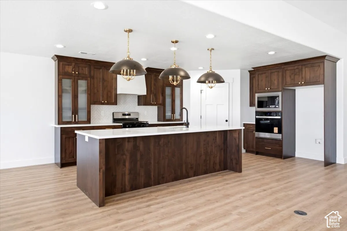 Kitchen featuring wood-finish flooring, dark wood cabinetry, white countertops, a built-in oven, and a kitchen island with pendant lighting