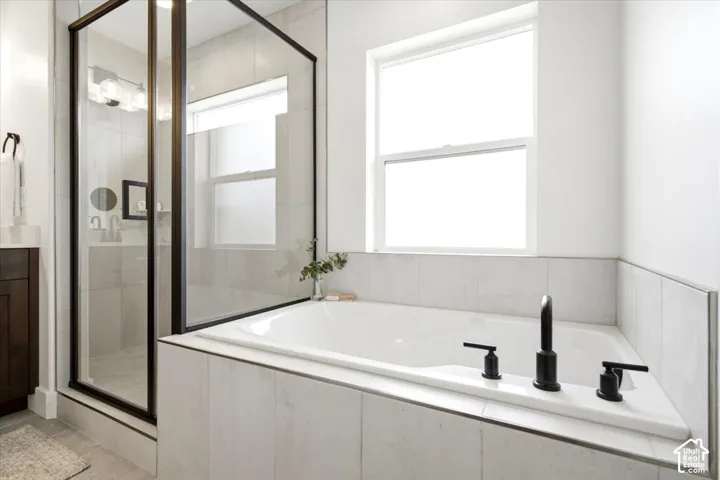 Built-in soaking tub with matte black fixtures, white tile surround, and a clear glass shower enclosure with black trim