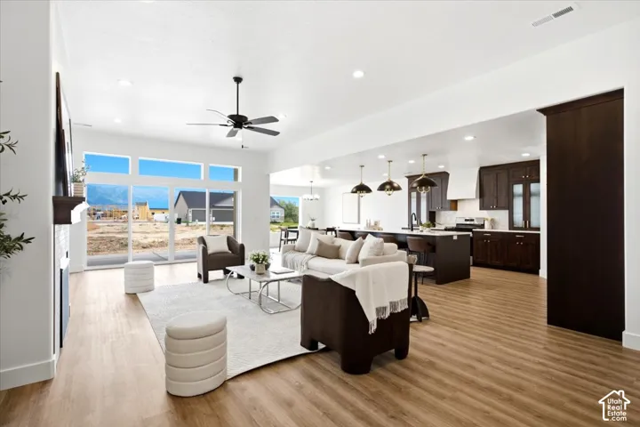 Spacious open-concept living area featuring wood-finish flooring, a ceiling fan, and large windows