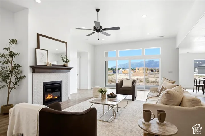 White tile fireplace with wood-finish mantel, large sliding glass doors, recessed lighting, ceiling fan, and wood-finish flooring