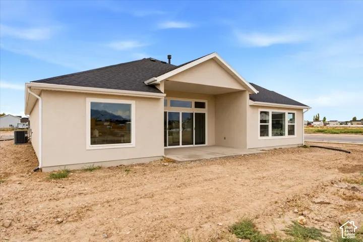 Rear exterior with light-colored stucco finish, dark shingle roof, and white-framed windows