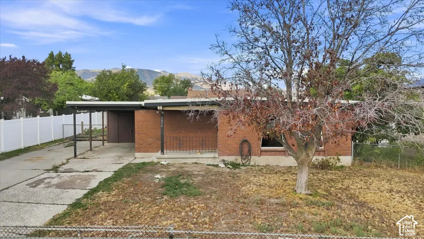 Brick exterior with a covered carport, concrete driveway, and white privacy fencing