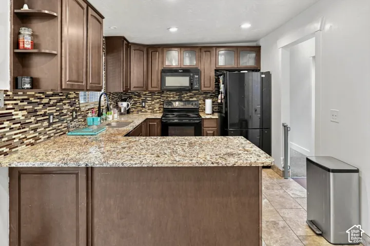 U-shaped kitchen featuring wood cabinetry, granite countertops, a mosaic tile backsplash, and stainless steel appliances