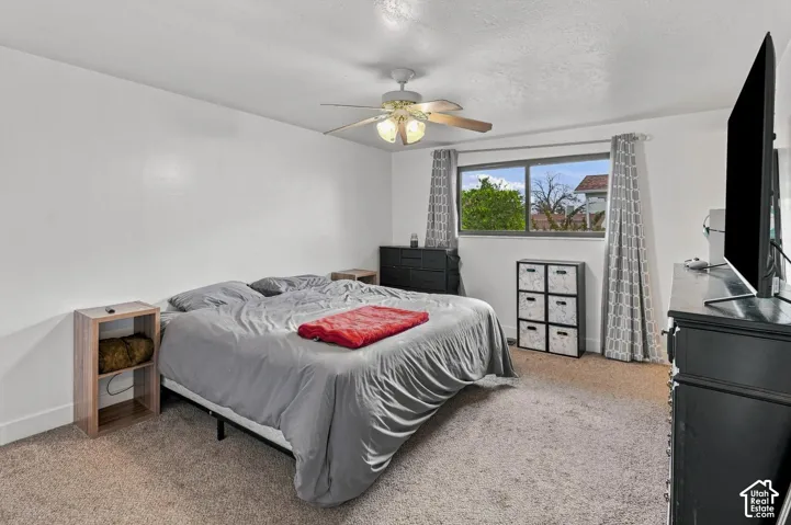 Carpeted bedroom featuring a ceiling fan with integrated lighting and a window