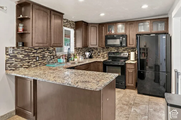 Kitchen featuring wood-finish cabinetry, patterned tile backsplash, granite-style countertops, and a black appliance package
