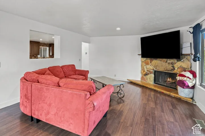 Stone-clad fireplace with hearth, wood-finish flooring, white walls, and pass-through opening to an additional room