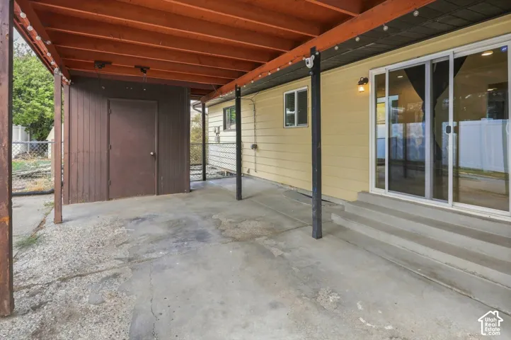 Covered patio with exposed wood ceiling, concrete flooring, and an integrated storage shed