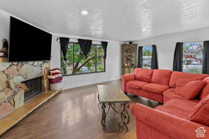 Spacious living area featuring a stone-clad fireplace and hearth, wood-finish flooring, recessed lighting, and large windows